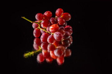 A bunch of grapes placed on the mirror with a black background