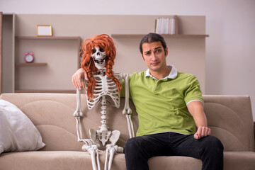 Young man sitting on the sofa with female skeleton