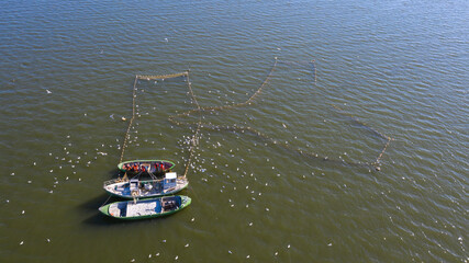 Aerial view to the sea with the fish traps and fishers loading their Baltic Herring catch to their boats and attracted by seagulls 