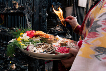 Offerings plate of Hindu devotee in Bhaktapur, Nepal. Select focus on the lighter part of the plate. Woman lighting oil lamp. Religion. Low light.
