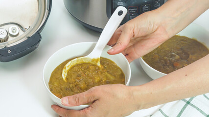 Creamy lentil soup cooked in multi cooker close up in a bowl, woman hands, white background