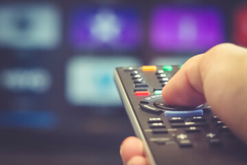 TV remote control in hand with blurred streaming media service in the background