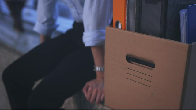 Stressed and worried young Asian woman with box of items sitting alone after being laid off from job due to covid-19 pandemic
