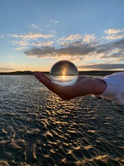 Hand holding a glass crystal ball on the beach at sunset