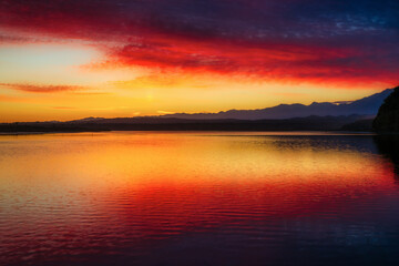 Fototapeta na wymiar Amazing red and yellow sky colour reflected in Okarito Lagoon with a backdrop of the Southern Alps at Dawn
