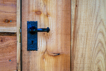 Closeup of black wrought iron door handle on waney edge wooden shed door.
