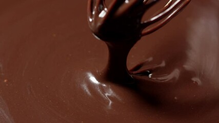 Close-up chef stirring, mixing melted liquid premium dark chocolate with a whisk. Slow motion. Preparation of premium handmade candies, desserts. Video blog about sweets. World Chocolate Day concept