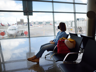 Young woman traveler wearing face mask waiting a departure of fligh in a lounge of airport