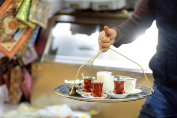 The waiter of outdoors cafe is serving tray with glasses of traditional turkish tea and milk....