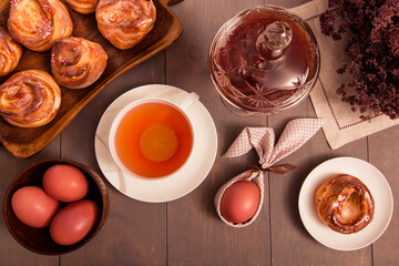 Easter breakfast. Still life with colored eggs, tea with lemon in a white cup, muffins. On the table is a glass vase with sweet, strawberry jam and a bouquet of flowers. Gray wooden background.