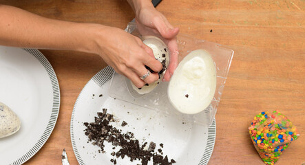 Filling molds with melted white chocolate and cookie pieces to prepare Easter eggs