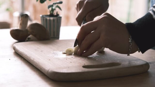 Woman hands slicing garlic with a steel knife on a chopping board