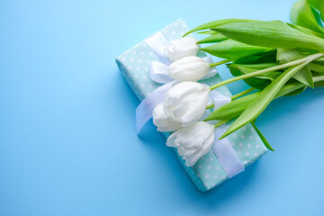 Obraz na płótnie Canvas Present and flowers white tulips on blue background.women day. Mother day .Spring flowers.Gift with white ribbon.