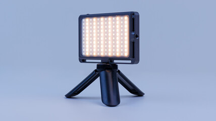 Small-sized LED lamp for photo and video production. It stands on a tripod, is illuminated and illuminates. Soft focus.
