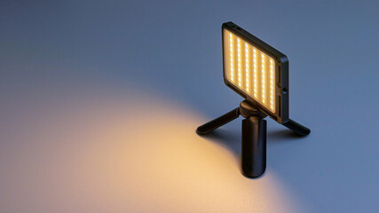 Small-sized LED lamp for photo and video production. It stands on a tripod, is illuminated and illuminates. Soft focus.