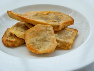 Fried sliced ​​sweet potatoes served in a white bowl on a white tablecloth, Dominican dish.
