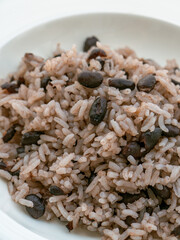 Rice with black beans served in a white bowl on a white tablecloth, widely consumed in the Dominican Republic and known as moro.