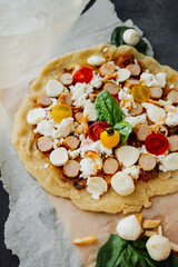 raw homemade pizza with chicken, tomatoes, mazzarella cheese and basil on a dark table with baking paper. food content for a blog about ordinary simple home-made food. selective focus
