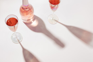 Bottle of rose wine and two crystal glasses on light background with hard sunlight at summer sunny day