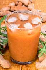 glass of tamarind water with ice cubes and whole tamarinds on the side. traditional mexican drink made from tamarind pulp. in close up view