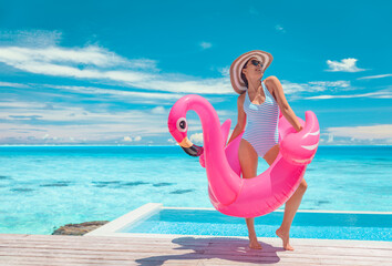 Summer pool fun swimsuit model posing in pink flamingo float showing off slim figure bikini ready body for luxury Caribbean vacation getaway. Woman having fun by hotel infinity pool. © Maridav
