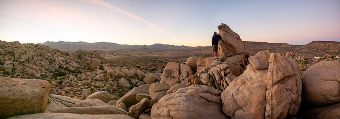 Panorama of man hiking among field of boulders at dusk with sunset sky  Yucca Valley, California near Joshua Tree National Park on a sunny January day with dramatic sky