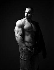 Fototapeta na wymiar Black and white. Brutal muscular man, athlete, weightlifter stands in jeans and shirtless and looks aside over dark background