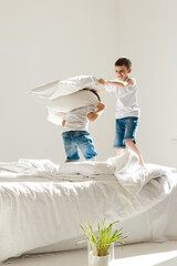 Indoor positive activity. Small children jumping on a bed and having fun fighting with pillows in sunshine