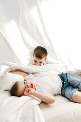Fototapeta premium Indoor positive activity. Small children playing on a bed and having fun in sheet hut
