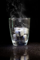 stainless steel cubes simulating ice in whisky glass on a black table.