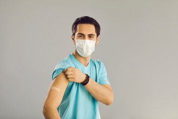 Vaccination of the population. Close up on gray background man in medical mask shows hand with patch at vaccine injection site. Young man received a vaccine against the corona virus.