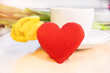 Red heart on the background of a white cup with a yellow tulip.