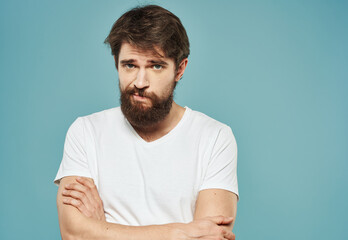 a man in a white t-shirt on a blue background gestures with his hands sad look