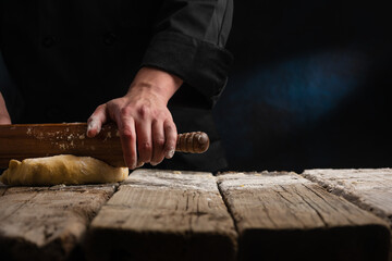 Chef prepares dough with rolling pin on black background.Culinary pastries, dough preparation. Freezing in motion. Recipe book on a black background for advertising baking and restaurant business