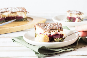 A broken piece of cake on a saucer, on a green napkin, without eggs and gluten, with a cream and strawberry layer, on a light wooden background.