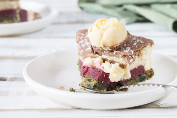 A broken piece of cake on a saucer close-up, without eggs and gluten, with a cream and strawberry layer, on a light wooden table.