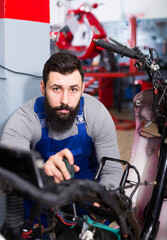 Fototapeta na wymiar Smiling male worker fixing failed motorcycle in motorcycle workshop