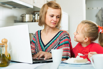 portrait of female freelancer working at notebook, little girl eating nearby