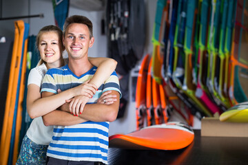 Young smiling american couple is posing in surfboard store on the beach..