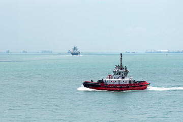 Tugboat on her way to assist with maneuverings, to cargo ship arriving to port of Singapore.