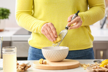 Woman grating ginger at table in kitchen
