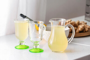 Glasses and jug of healthy ginger juice on table in kitchen
