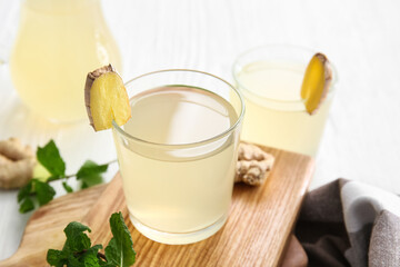 Board with glass of healthy ginger juice on light background