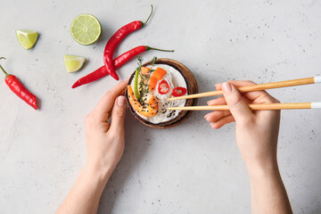 Woman eating Thai noodle soup on light background