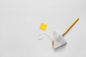 Spoon with tea bag on light background