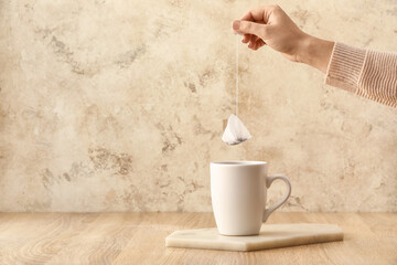Woman brewing tea with bag in cup on table