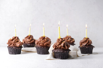 Tasty chocolate cupcakes with candles on light background