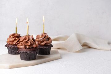 Tasty chocolate cupcakes with candles on light background