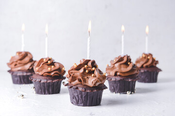 Tasty chocolate cupcakes with candles on light background