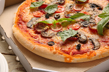 Cardboard box with tasty pizza on wooden background, closeup